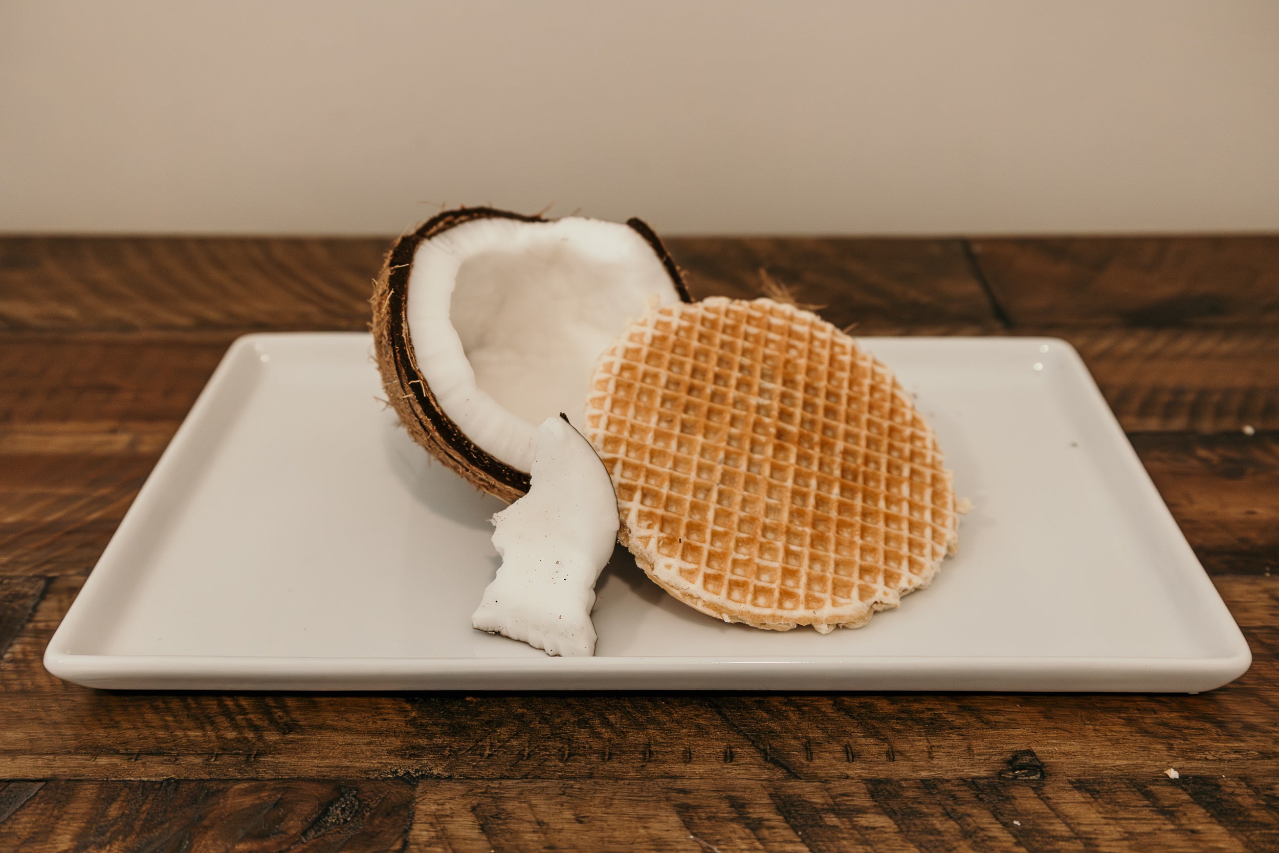 Coconut half and waffle cookie on a white plate with a wooden background