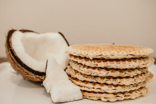Stack of waffle cookies with a halved coconut on a neutral background