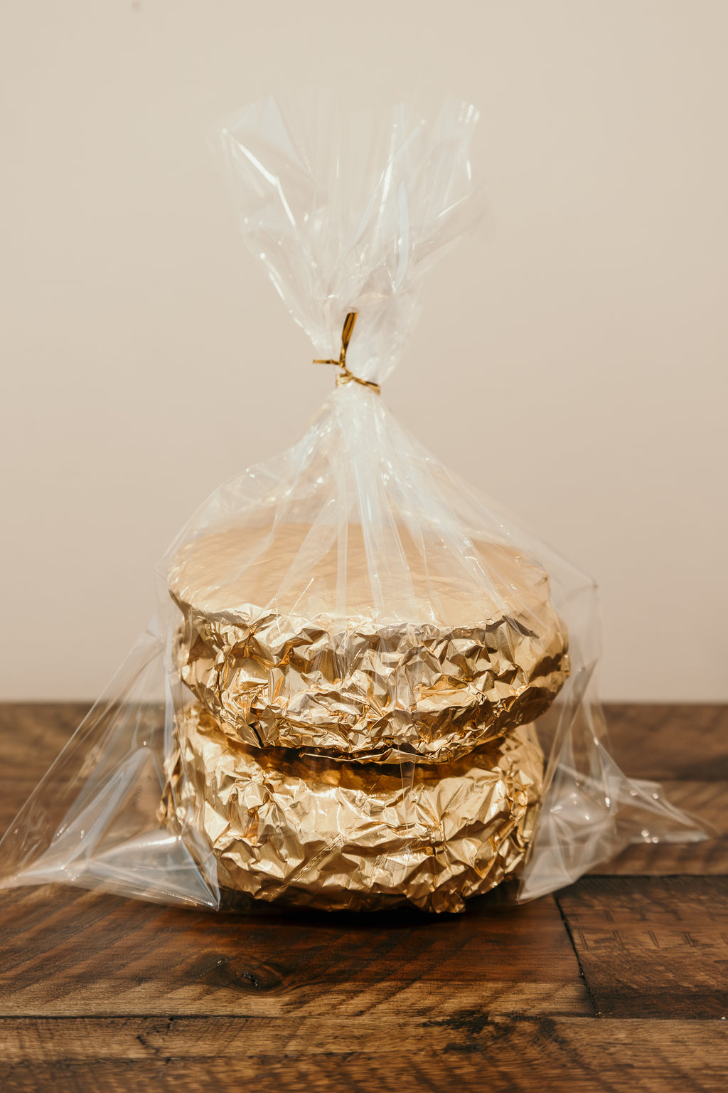 Stack of gold-wrapped waffles in clear cellophane on a wooden surface with a neutral background