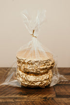 Stack of gold-wrapped waffles in clear cellophane on a wooden surface with a neutral background