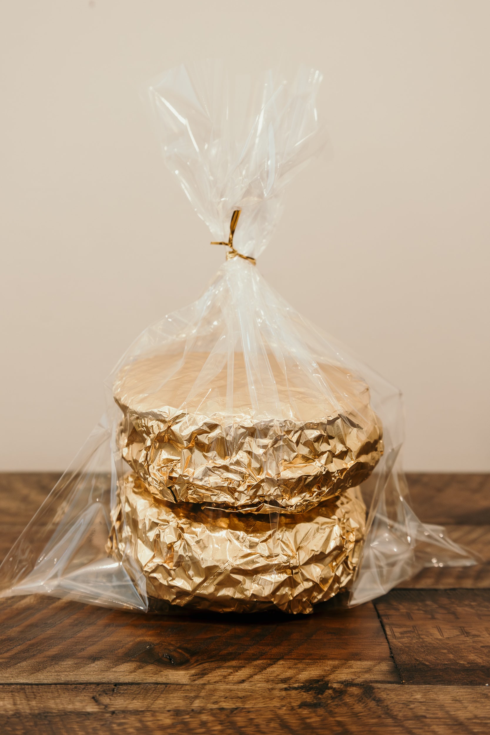 Stack of gold-wrapped waffles in clear cellophane on a wooden surface with a neutral background