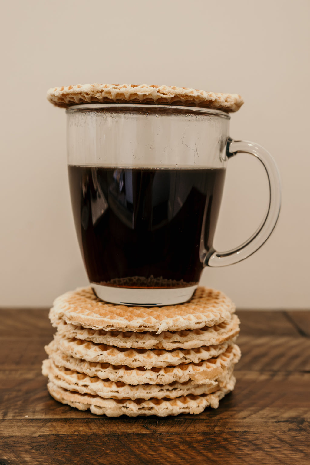 Clear mug with coffee on a stack of waffles on a wooden surface.